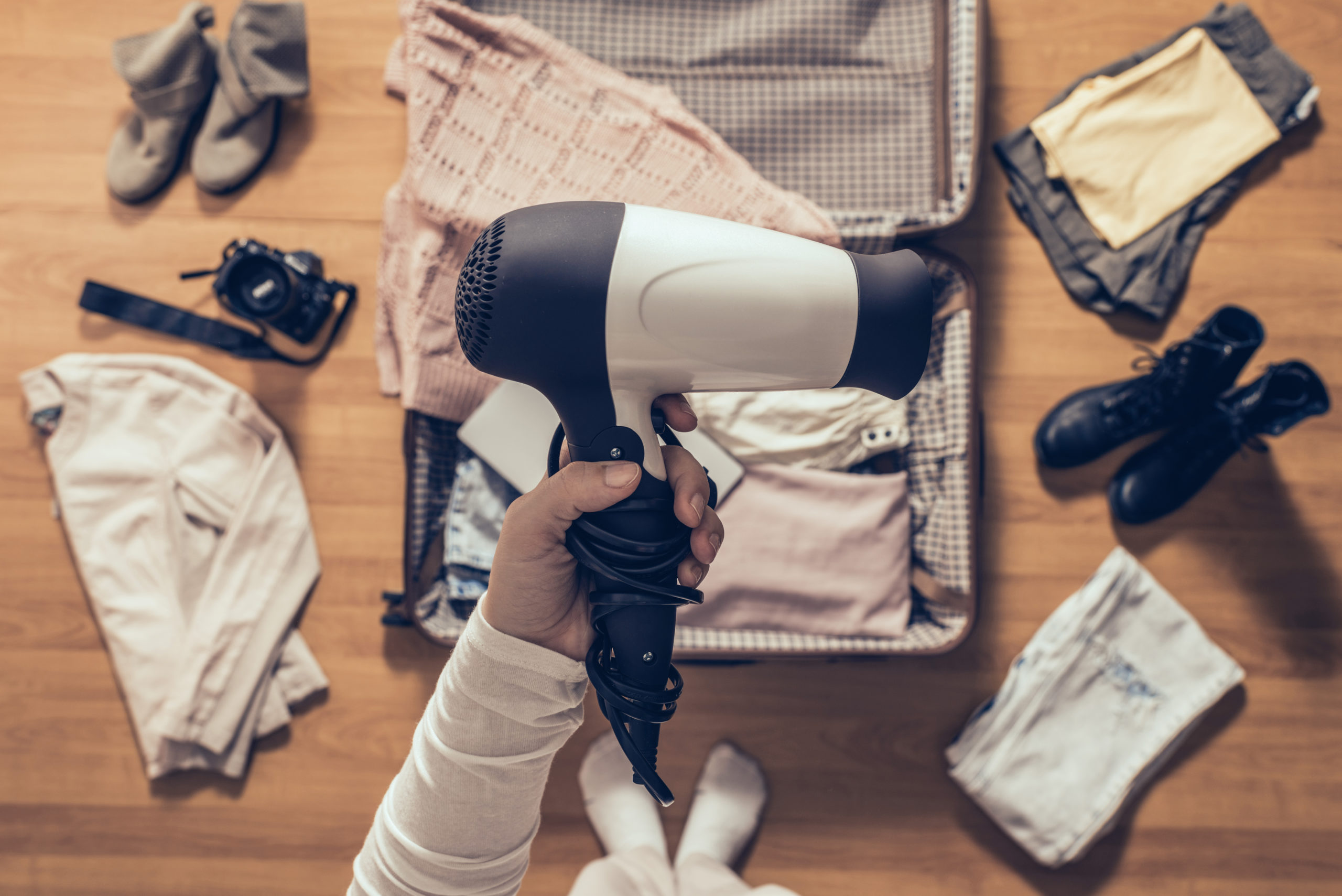 Person packing a travel hair dryer in a full suitcase