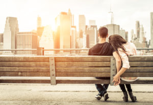 Couple sitting on a bench holding hands in front of the New York City skyline